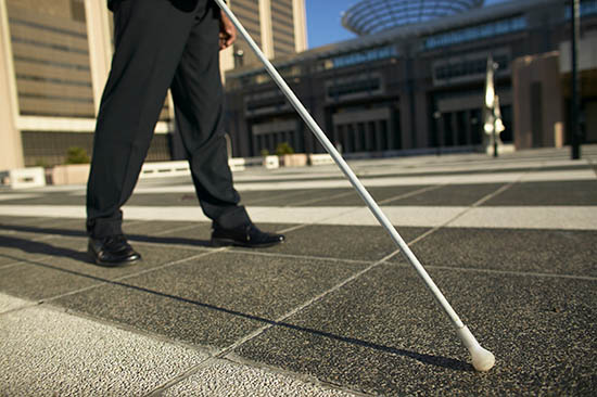 A man wearing business clothes walking with a white cane