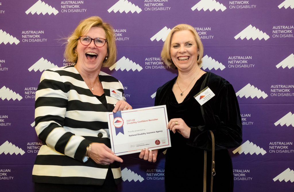 Corene Strauss standing with Donna Purcell, with big smiles holding an award. Purple Australian Network on Disability banner behind them.